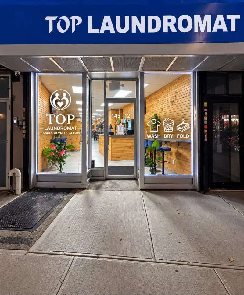 TOP Laundromat storefront at night: blue sign, number 145-12 above the door, and the wash, dry, fold icons on the window